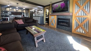 A modern living room with a fireplace, a television, and a kitchen in the background. - Seven Springs Slope-Side Home, Ski right to the Lift #1  Boomerang Trail. (Champion)