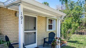 Une maison avec un porche, un paillasson, une porte moustiquaire et un banc.