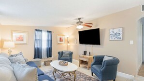 Un salon comprenant un canapé, des fauteuils, une table basse, un téléviseur et un ventilateur de plafond.