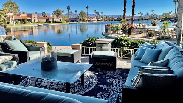 A poolside area with outdoor furniture, a view of a lake, and palm trees.