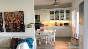 A modern kitchen with white cabinets, a dining area with a white table and chairs, and a ceiling fan.