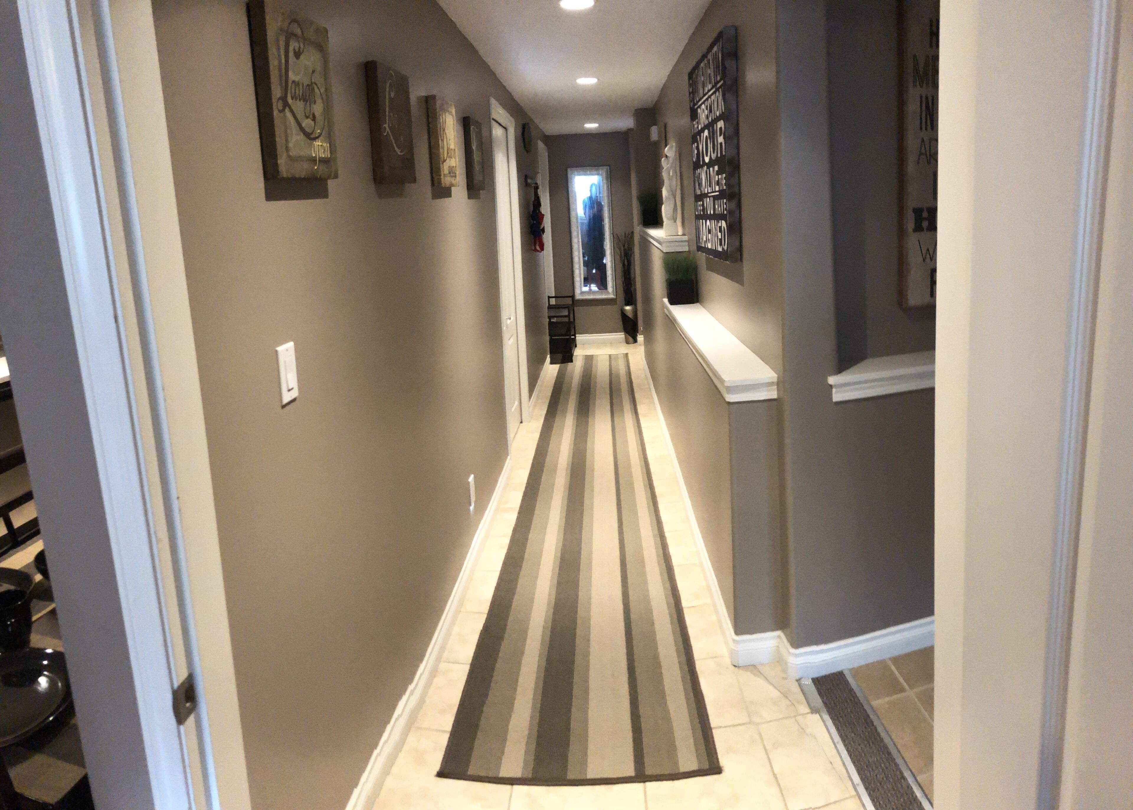 A hallway with a striped rug, framed artwork on the walls, and a statue on a pedestal.