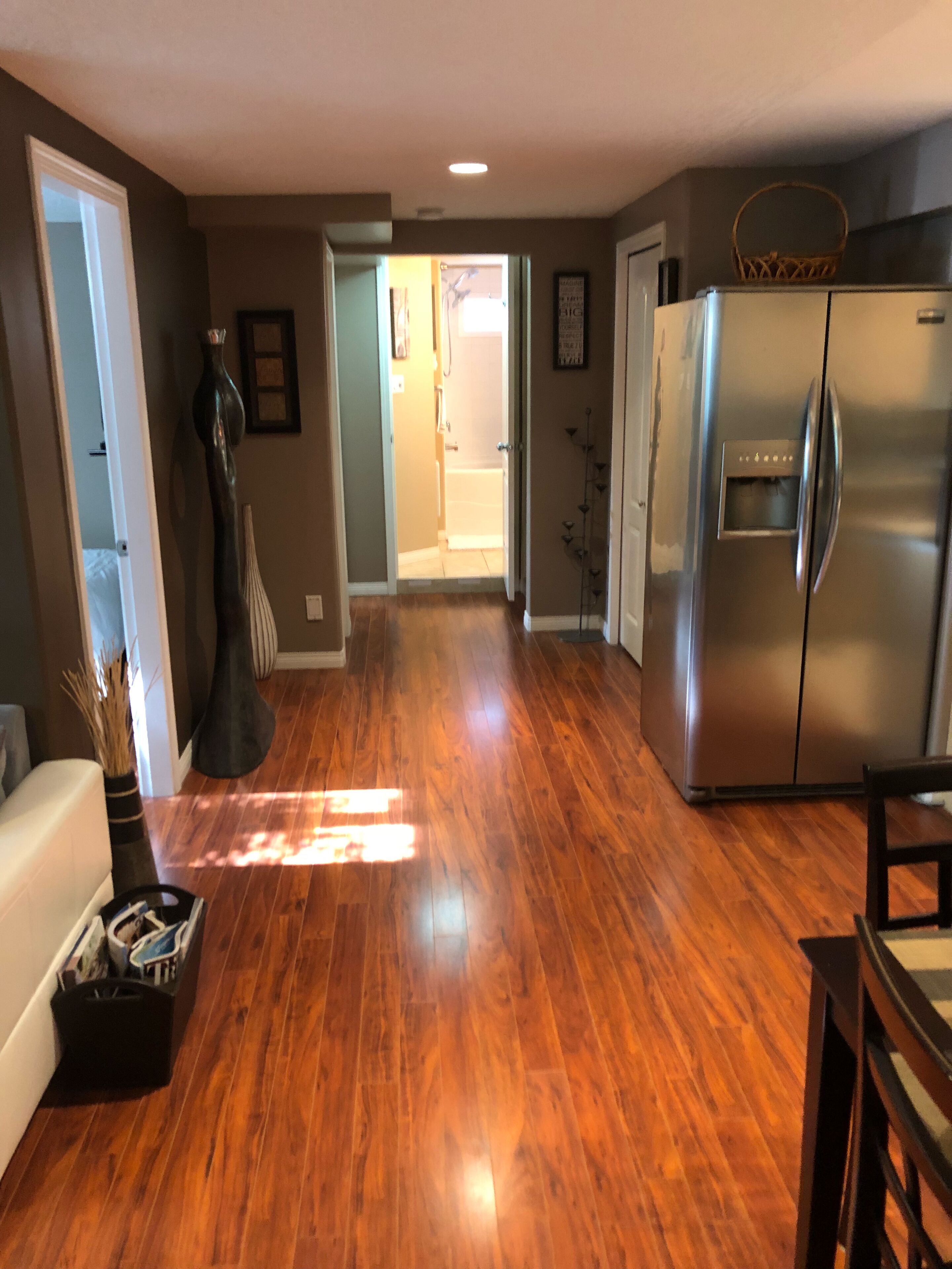 A kitchen with a stainless steel refrigerator, wooden flooring, and a dining area with a table and chairs.
