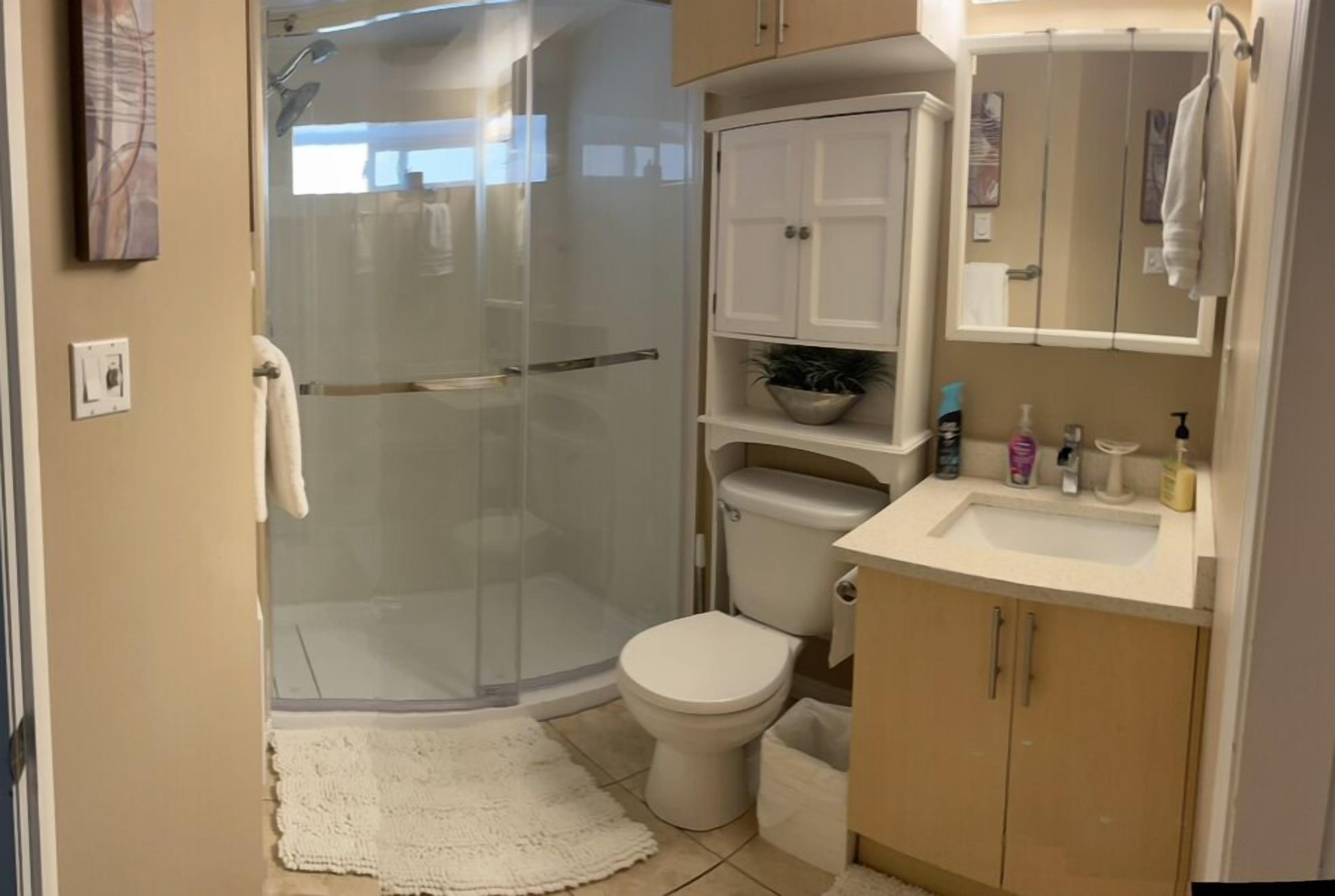 A bathroom with a glass shower enclosure, a toilet, a sink with toiletries, and a cabinet.