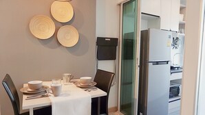 A dining area with a table set for four, a refrigerator, and a sliding glass door leading to a kitchen. - The Kith Plus Sukhumvit 113 (Samut Prakan)