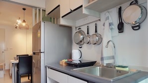 A compact kitchen with a sink, stove, and hanging pots. There is a dining area with a table and chairs. - The Kith Plus Sukhumvit 113 (Samut Prakan)