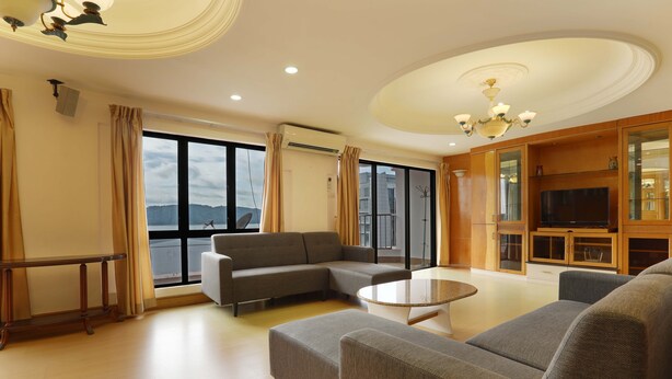 A spacious living room with a large sectional sofa, a round coffee table, and a television on a wooden cabinet. - 1st Choice Vacation Apartments at Marina Court Resort Resort (Kota Kinabalu)
