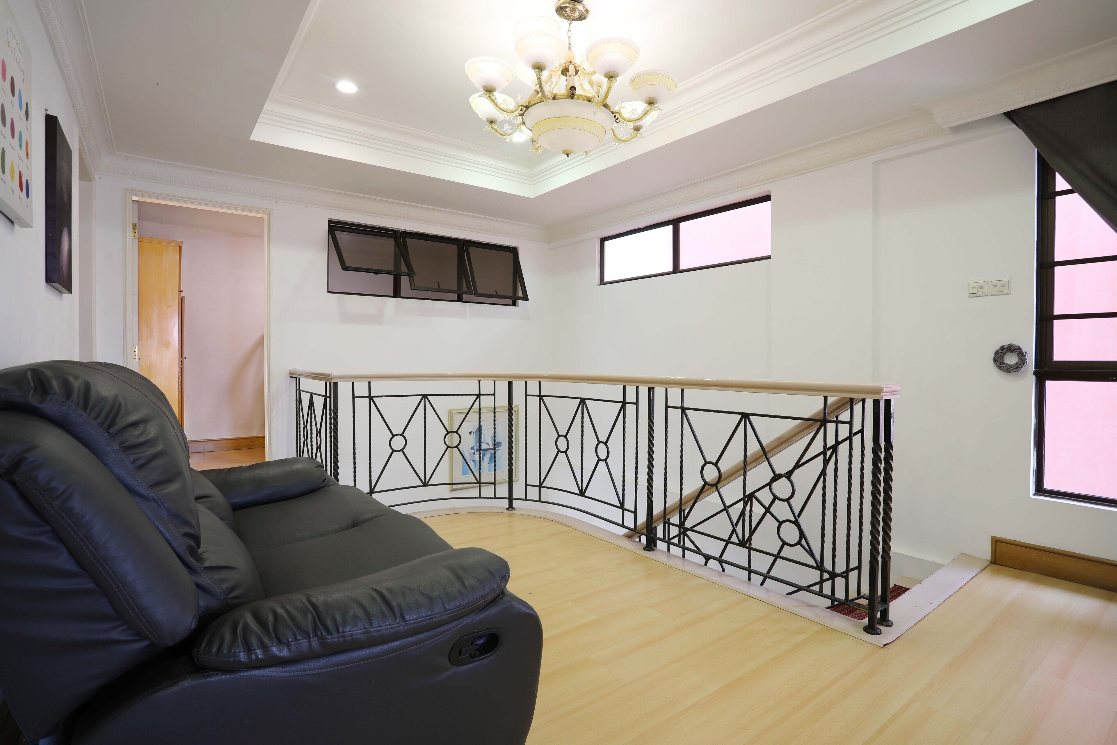 A spacious room with a black leather sofa, a wooden staircase with a black railing, and a chandelier.