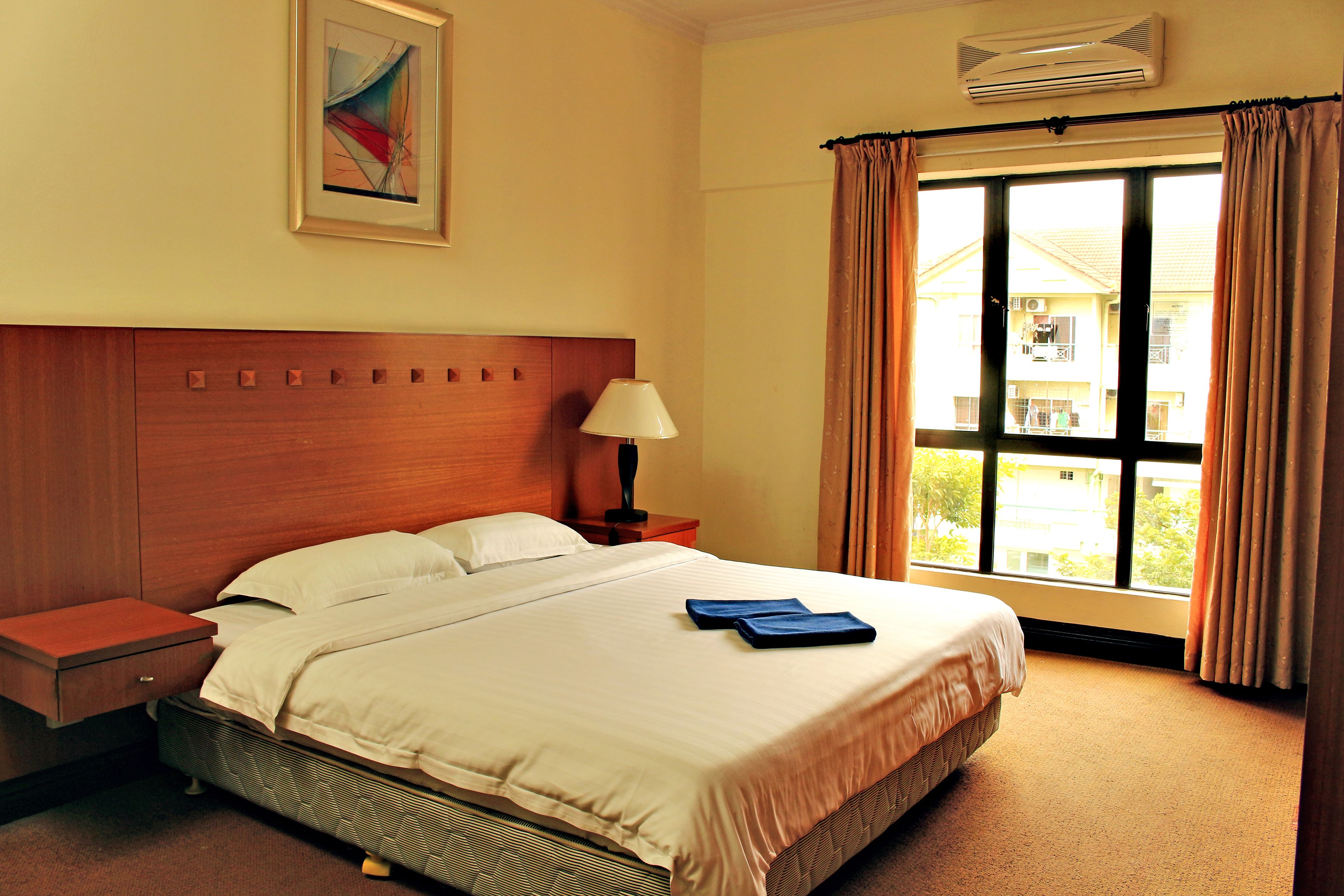 A neatly made bed with a wooden headboard, a bedside table with a lamp, and a window with curtains.