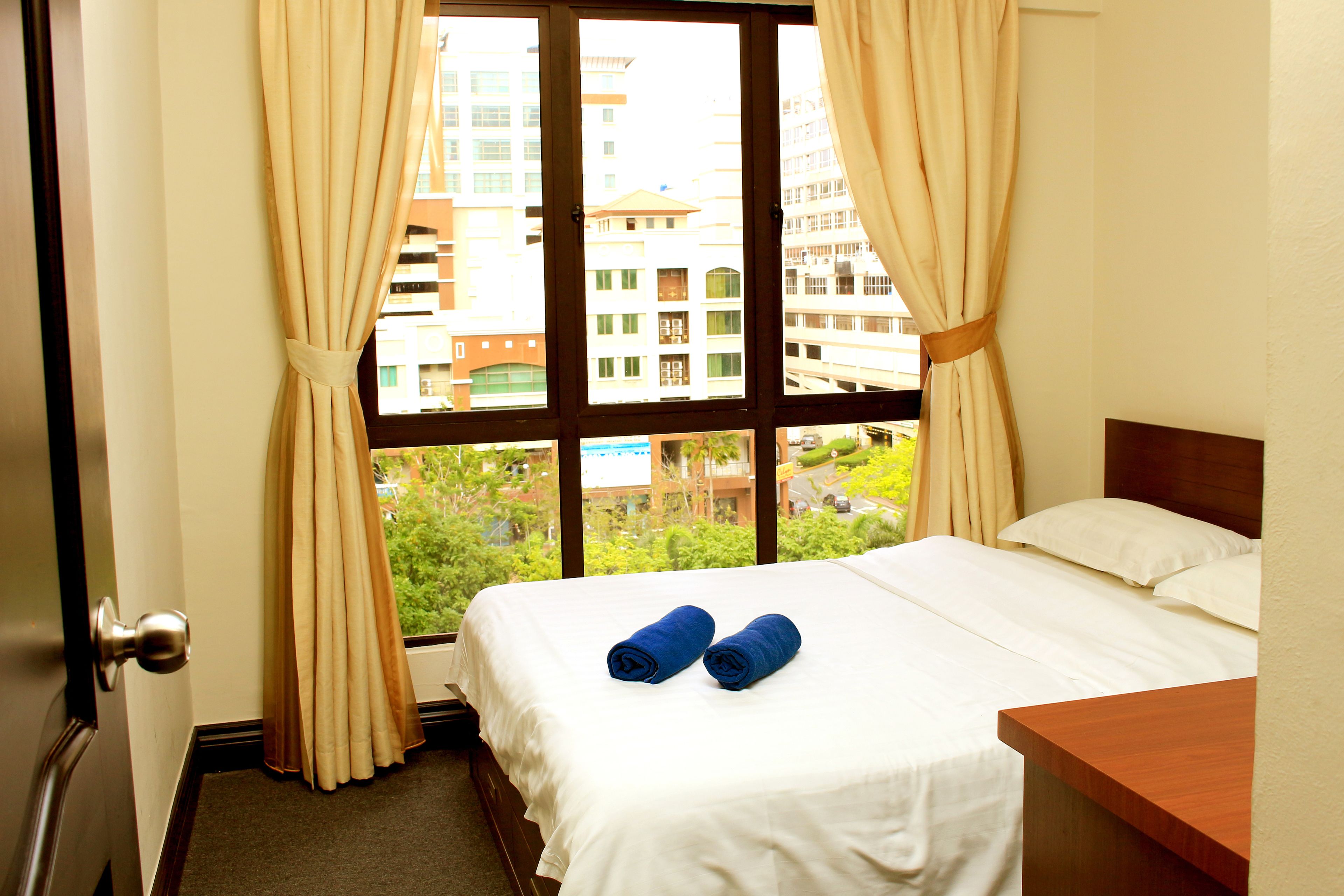 A hotel room with a bed, a wooden nightstand, and a window with curtains.