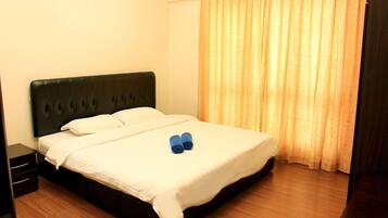 A neatly made bed with white linens and two rolled towels, a dark headboard, and a wooden floor.
