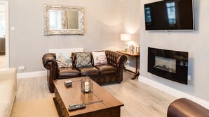 Una sala de estar con un sofá de cuero marrón, una mesa de centro de madera, una chimenea, un televisor y un espejo en la pared.