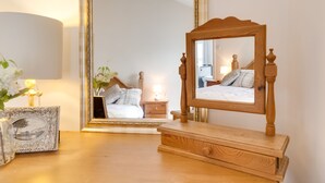 Un dormitorio con un aparador de madera, una mesita de noche con lámpara, un espejo enmarco y una planta en la mesita de noche.