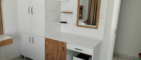 Un dormitorio con un armario blanco, un aparador de madera, una mesita de noche y un espejo.