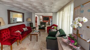 A spacious living room with a red sofa, green armchairs, and a coffee table. There is a mirror on the wall, a lamp, and a bulletin board with notes. - Alibabam Apart Hotel (Kusadasi)
