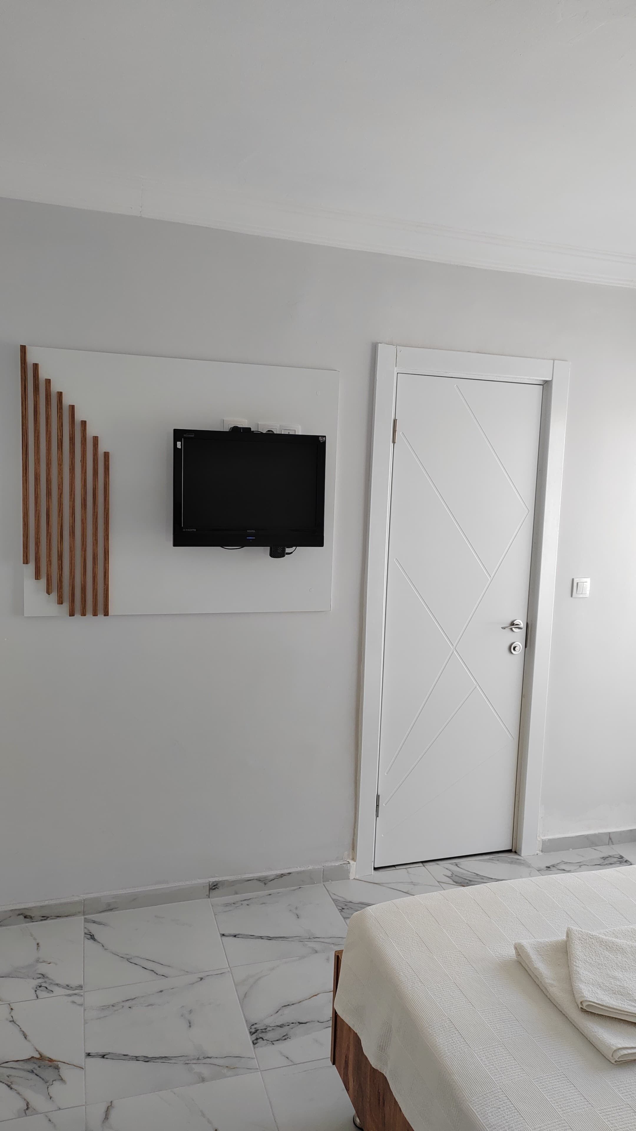 A bedroom with a bed, a television mounted on the wall, a door, and a patterned floor.