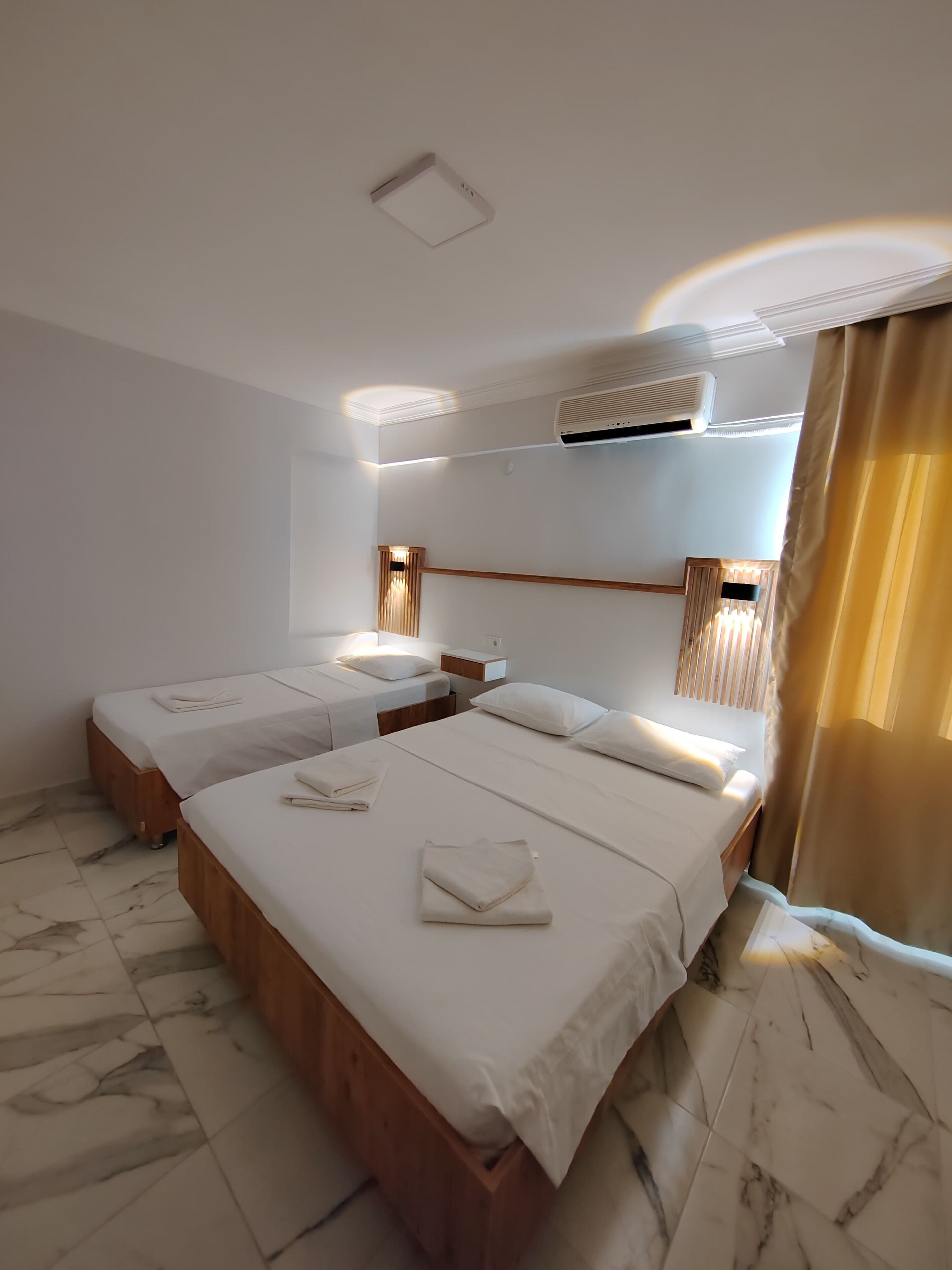Ett hotellrum med två sängar, ett marmorgolv, en luftkonditioneringsanläggning och ett fönster med gardiner.