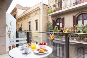En balkon med et bord dækket til morgenmad, inklusive croissanter, frugt og juice.