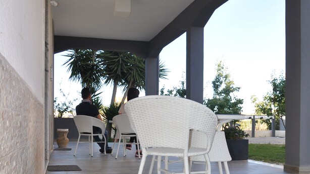 A covered patio area with white wicker furniture, a potted plant, and a view of the outdoors. - Alicata B&B La Dimora Del Vento (Licata)