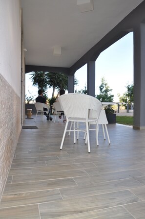 A covered patio area with white wicker furniture, a potted plant, and a view of the outdoors. - Alicata B&B La Dimora Del Vento (Licata)