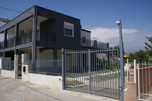 A modern two-story building with a gated entrance, balconies, and a clear sky.