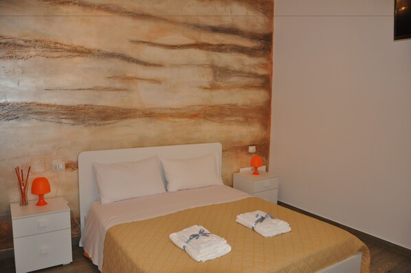 A hotel room with a bed, two nightstands, a wall with a textured design, and two towels on the bed.