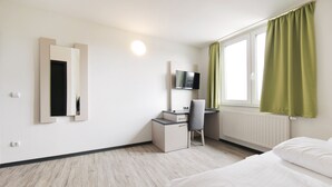 Een hotelkamer met een bed, een bureau met stoel, een aan de muur bevestigde televisie en een raam met gordijnen.
