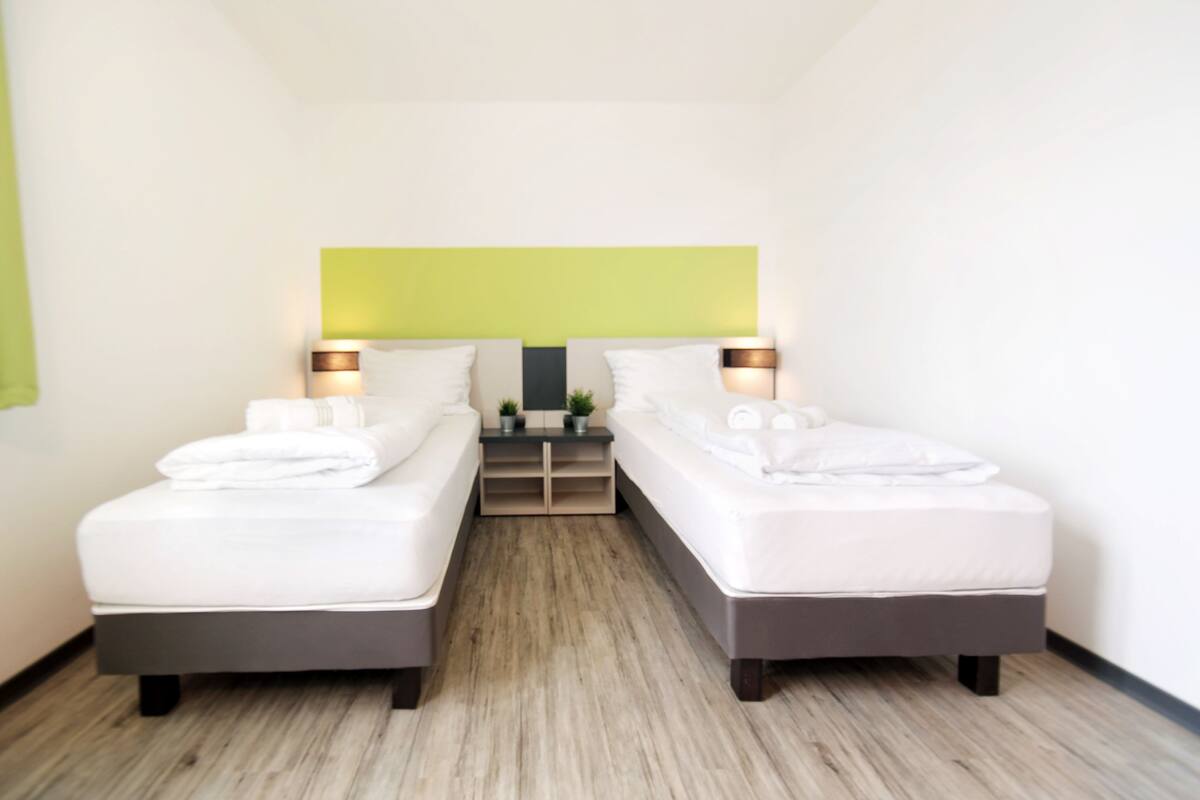 Een hotelkamer met twee bedden, een groene accentmuur en bedlampen.