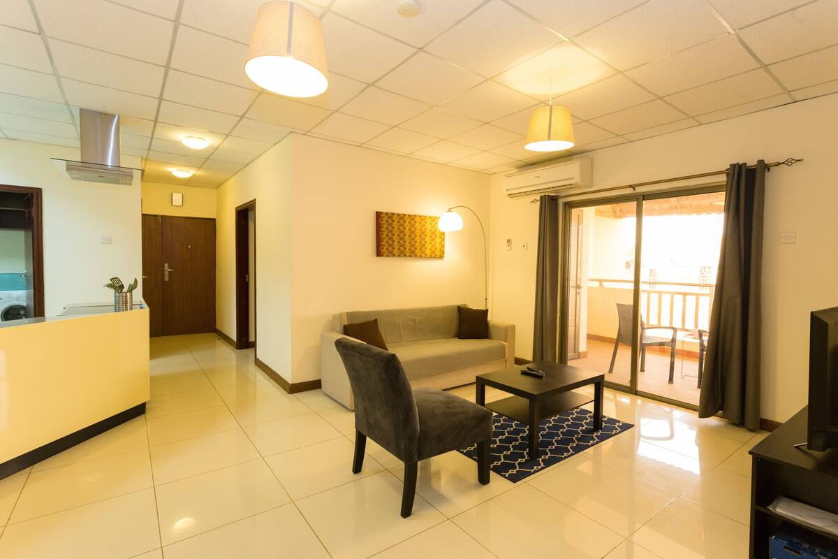 Una sala moderna con sofá, una silla, una mesa de centro y televisor. Cuenta con una zona de cocina con mostrador y pileta. El espacio tiene un balcón con vistas.