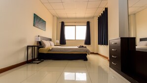 A hotel room with a bed, bedside tables, a dresser, a window with curtains, and a wall art piece.