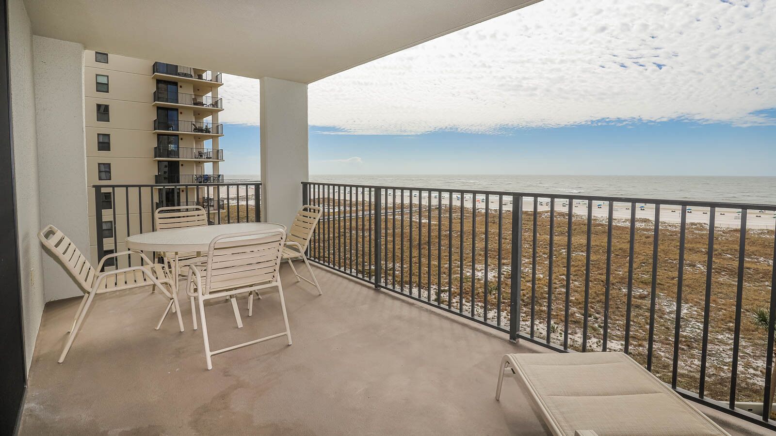 A balcony with a table and chairs, overlooking a beach with a fence.