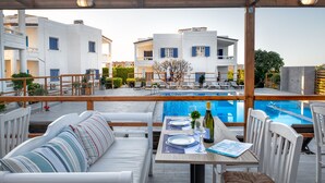 A rooftop terrace with a pool, white furniture, and a view of the surrounding buildings. - Aelia Apartments (Hersonissos)