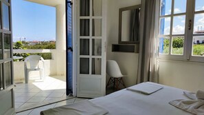 A hotel room with a balcony, a bed, a chair, and a window with curtains.