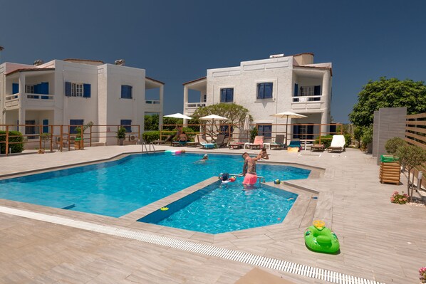 A swimming pool area with multiple pools, lounge chairs, and umbrellas. - Aelia Apartments (Hersonissos)