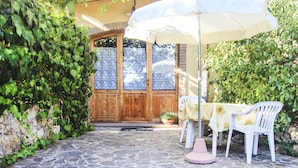 A stone-paved patio with a white umbrella, white chairs, and a table with a yellow tablecloth. - Podere Risoino (Poggibonsi)