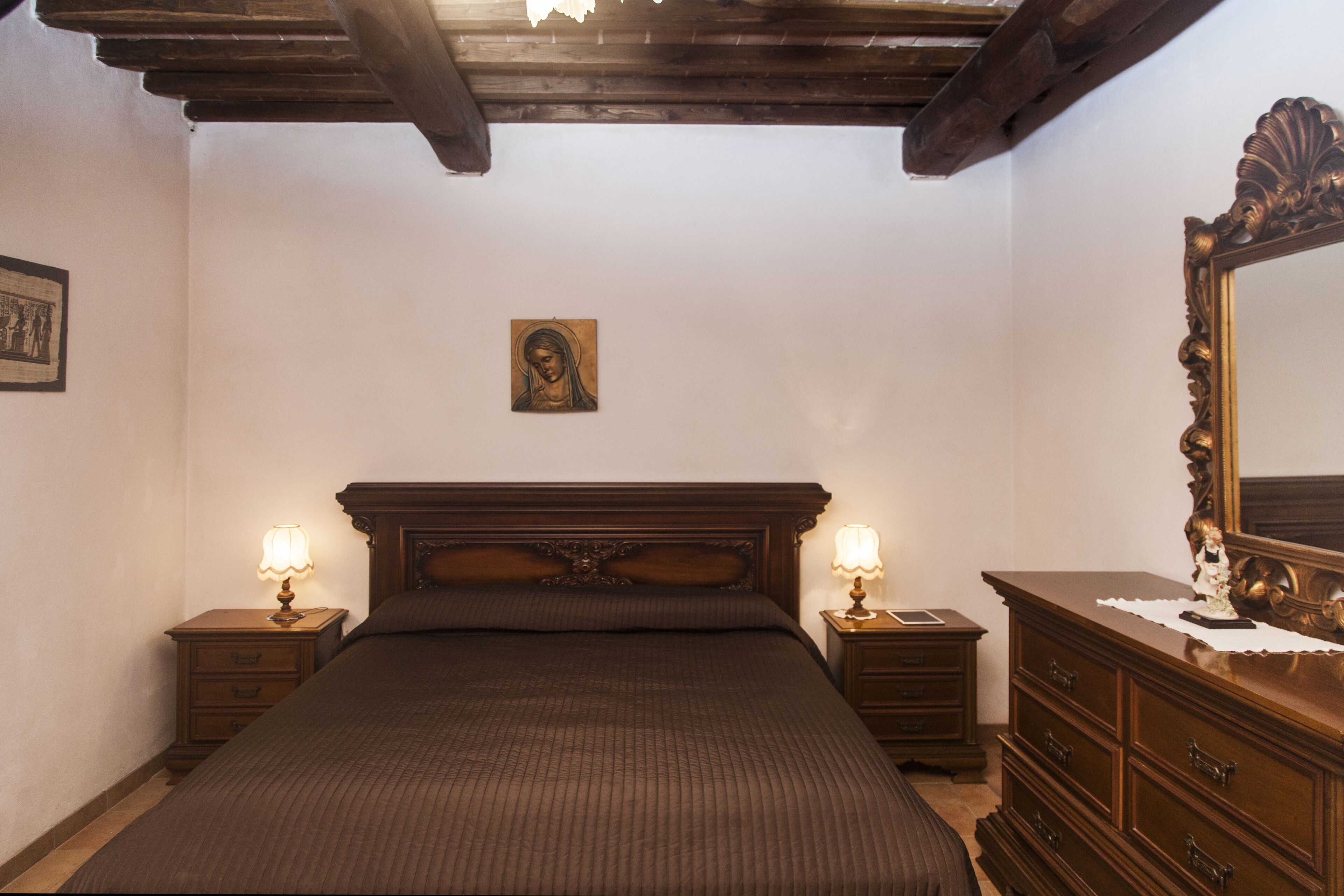 Ein Schlafzimmer mit einem großen Bett, einem hölzernen Kopfende, zwei Nachttischen mit Lampen, einer Kommode und einem Spiegel.