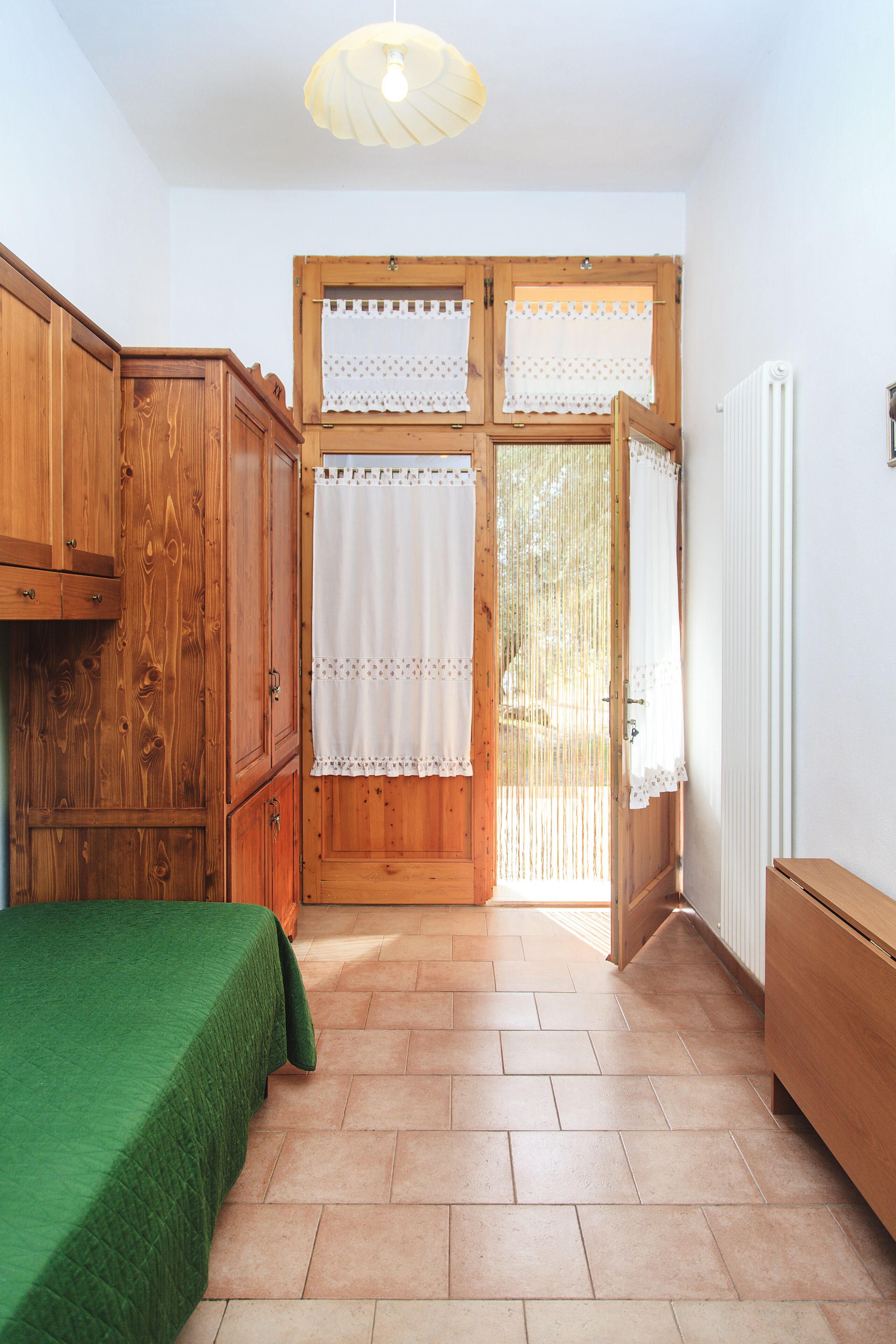 Una habitación con cama, armarios de madera, un radiador y una ventana con cortinas.