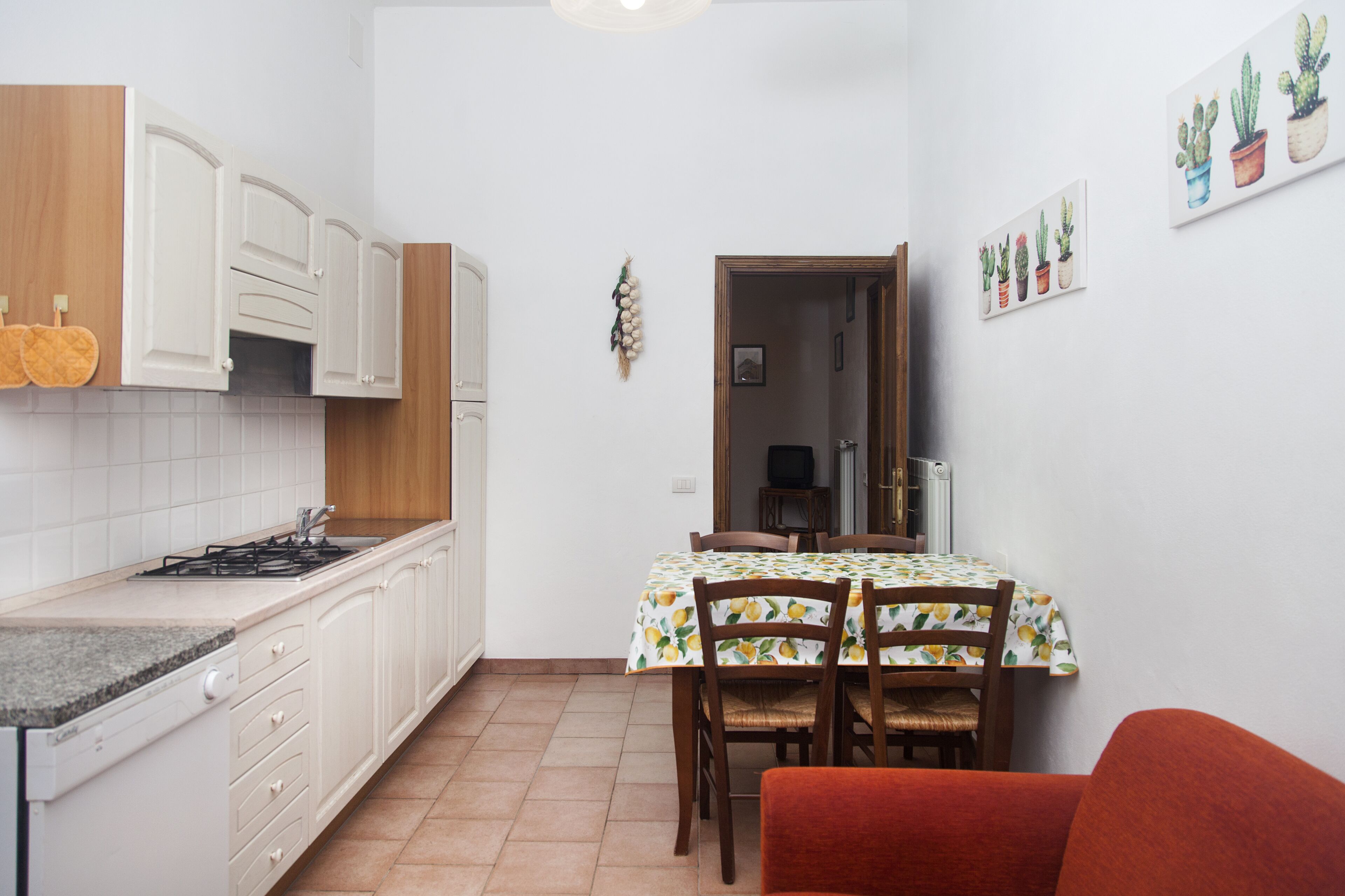 A compact kitchen with white cabinets, a dining table with chairs, and a red chair.