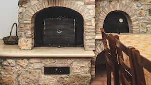 A stone fireplace with a wooden mantel, a rustic table, and chairs. - Podere Risoino (Poggibonsi)