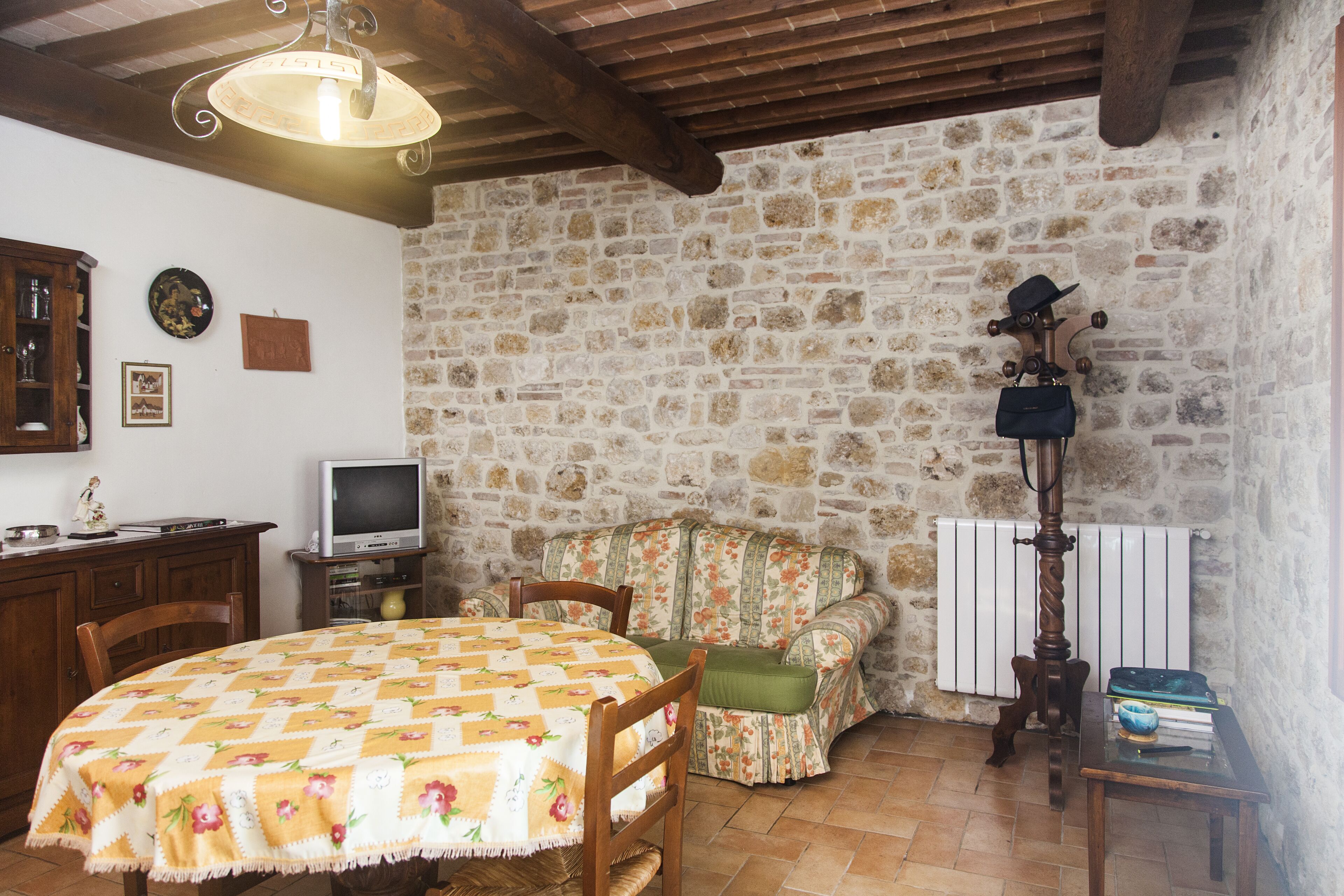 Una habitación rústica con pared de piedra, mobiliario de madera, una mesa con mantel floral y una radio antigua.