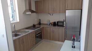 A modern kitchen with wooden cabinets, a stainless steel refrigerator, a microwave, and a sink. - Bela & Nunes (Lagoa)