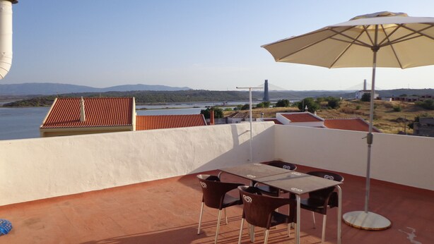A terrace with a table and chairs, an umbrella, and a view of a bridge and water. - Bela & Nunes (Lagoa)