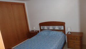 A bedroom with a wooden bed, two bedside tables with lamps, a wooden wardrobe, and a patterned bedspread. - Bela & Nunes (Lagoa)