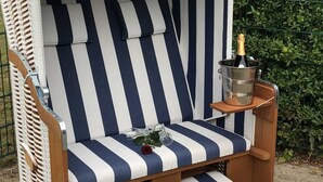 Una sedia da spiaggia a righe con un ombrellone, un tavolino e una bottiglia di champagne.