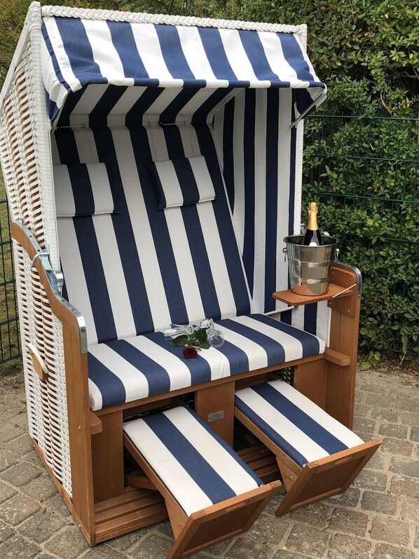 Une chaise de plage à rayures avec un parasol, une petite table et une bouteille de champagne.