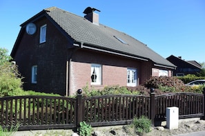 A two-story brick house with a dark roof, a wooden fence, and a small garden area.