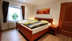 Una camera da letto con un letto in legno, un comodino con una lampada, una finestra con tende e un quadro appeso al muro.
