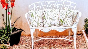 A white metal bench with a floral pattern, surrounded by potted plants and gravel. - Encanto Familiar (Penha)