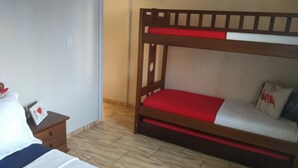 A room with a bunk bed, a bedside table with a lamp, and a door leading to another room. - Encanto Familiar (Penha)