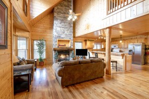 Cozy cabin living area with a stone fireplace, comfortable sofa, and modern kitchen.